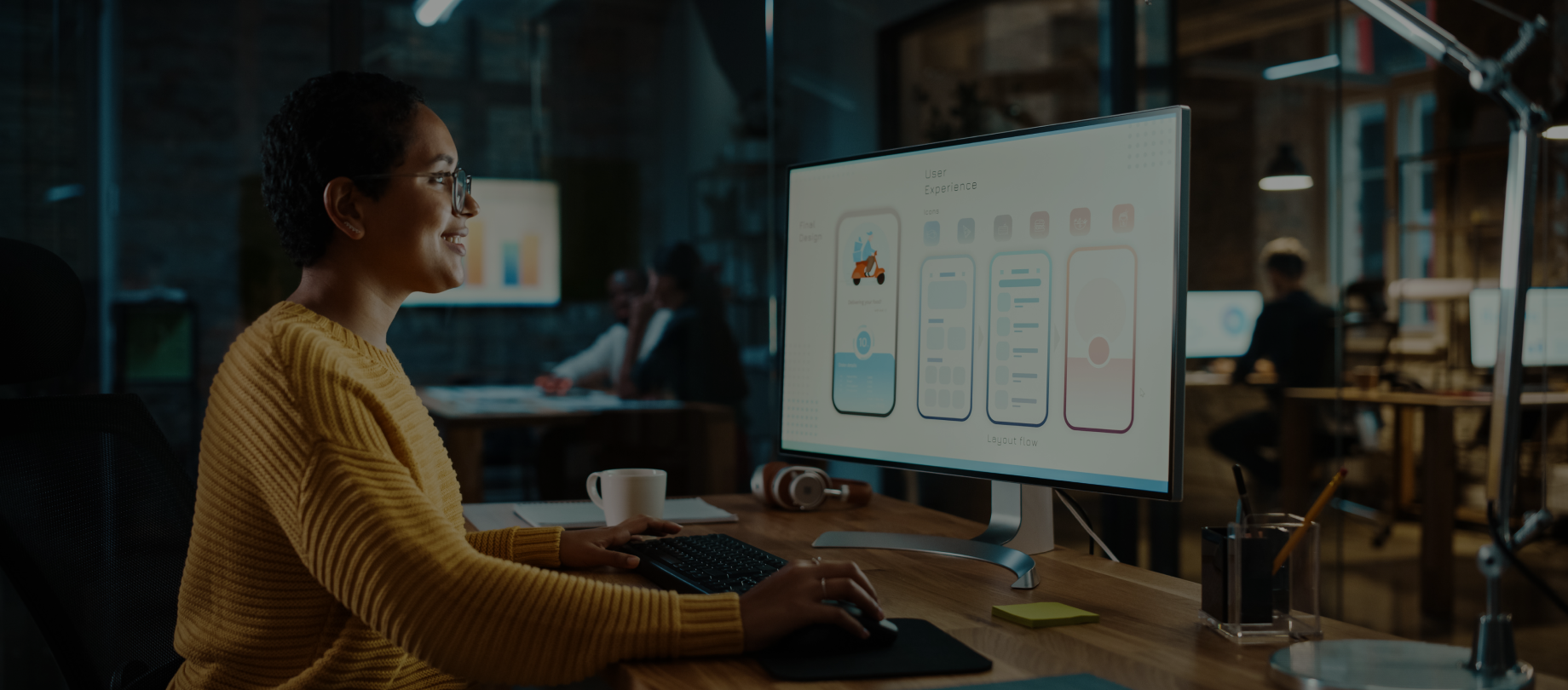 Female designer delivering UI/UX design services while working on a mobile app interface layout on a large monitor in a creative studio.
