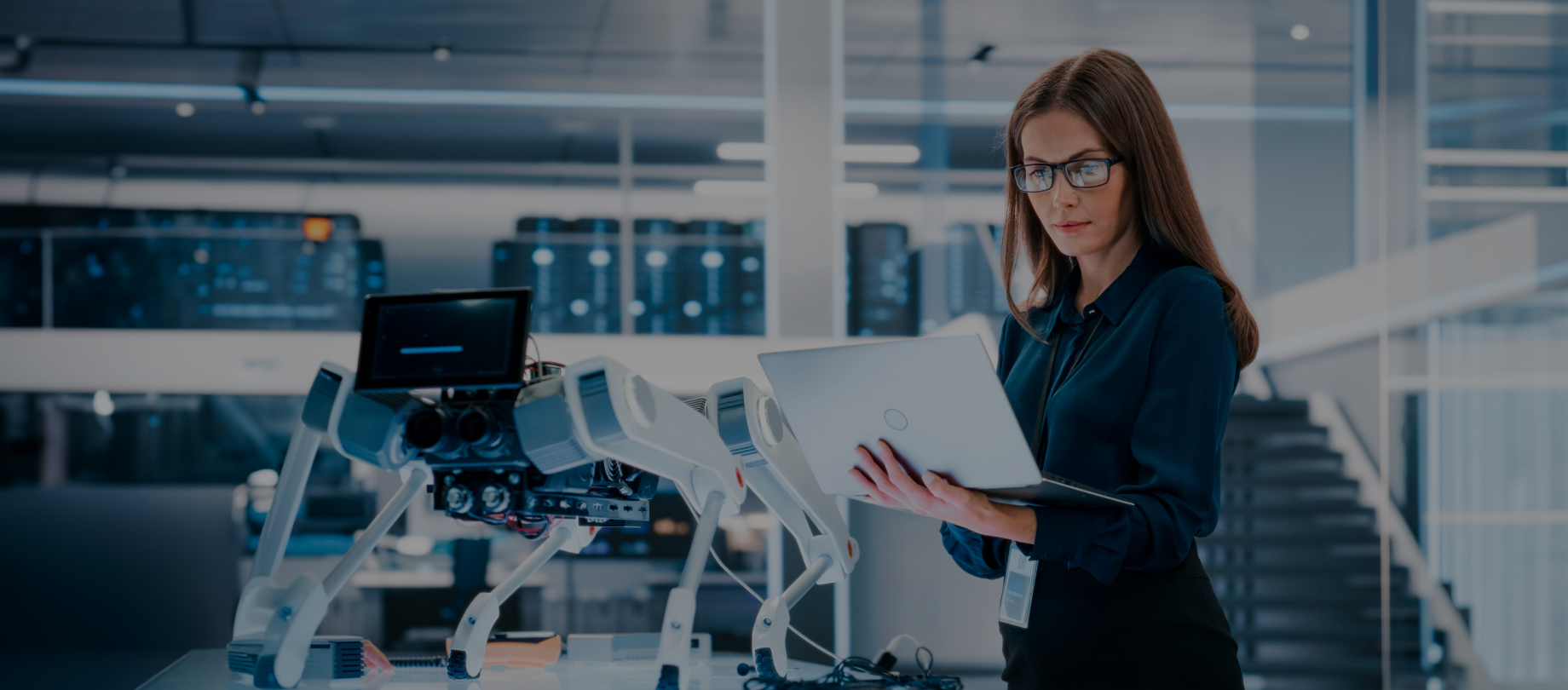 Female project manager delivering IT project management services while overseeing robotic equipment in a high-tech workspace.